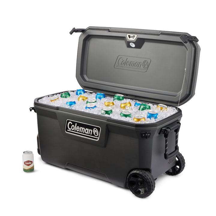 Black Coleman cooler with wheels filled with ice and bottles on a white background